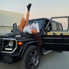 a woman laying on the hood of a black truck with her legs in the air