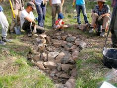 a group of people standing next to each other near rocks and dirt in the grass