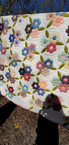 a person holding up a quilt with flowers on it in front of some trees and grass