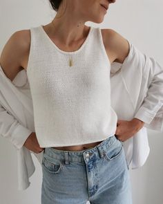 a woman with her hands on her hips wearing jeans and a white top, standing against a wall