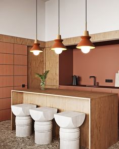 three white stools sitting in front of a counter with lights hanging above it and a potted plant on top