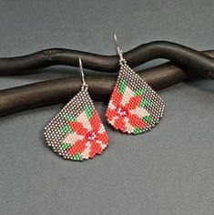 a pair of beaded earrings sitting on top of a black piece of wood next to a twig