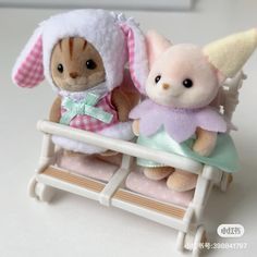 two small stuffed animals sitting on top of a white sleigh with pink and green accents