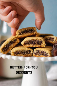 a person picking up some cookies from a white cake plate with the words, better - for - you desserts on it