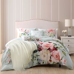 a bed with pink flowers on it in a bedroom next to a white dresser and lamp