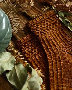 a knitted sweater and some leaves on a wooden table next to a blue bowl