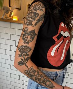 a woman with tattoos on her arm and chest standing in front of a tiled wall