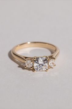 an engagement ring with three stones on the side and one stone in the middle, sitting on top of a white surface