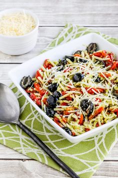 a white bowl filled with pasta and olives on top of a green towel next to a spoon