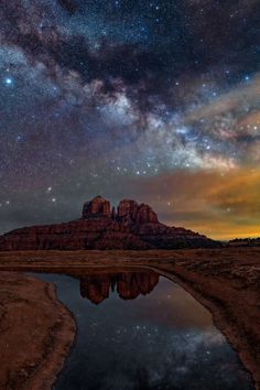 the night sky is filled with stars and clouds above a body of water that has a mountain in the background