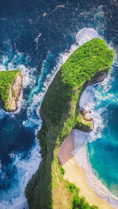 an aerial view of two green island shaped by the ocean water and sand, with waves crashing on them