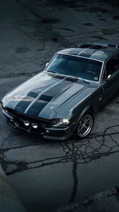 an old mustang muscle car parked in a parking lot with the hood up and stripes painted on it