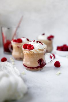 two dessert cups filled with whipped cream and raspberry toppings on a white surface