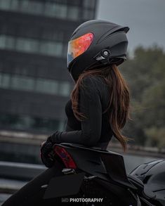 a woman sitting on top of a motorcycle wearing a black outfit and helmet with the sun reflecting off her face