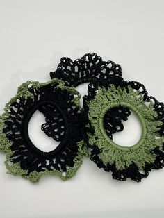 two crocheted black and green hair ties on a white surface with an oval hole in the middle