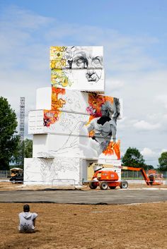 a man sitting on the ground in front of a tall building with paintings on it