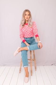 a woman sitting on top of a wooden stool in front of a white wall with her legs crossed