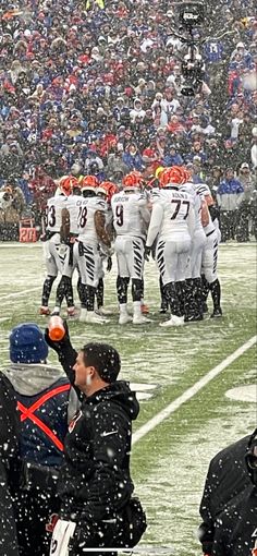 a group of football players standing on top of a field in the snow with people watching