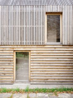 a wooden building with two windows on the side and grass growing in front of it