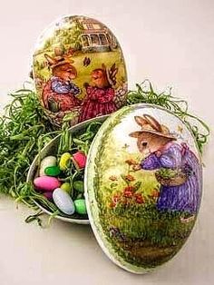 three decorated eggs sitting on top of green grass next to an egg box with some candy in it