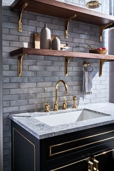 a kitchen sink with gold faucets and shelving above it