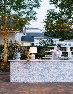 a woman standing at the bar in front of some trees with lights strung above it