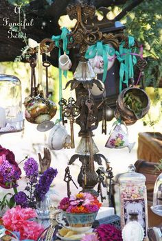 a table topped with lots of vases filled with purple and white flowers next to an ornate chandelier