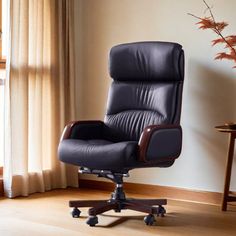 a black office chair sitting in front of a window next to a table with a vase on it