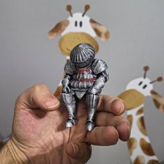 a hand holding a small toy in front of two giraffes on the wall