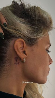 a woman with tattoos on her ear and behind her ear is a small rose tattoo