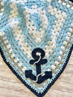 a blue and white crocheted blanket with an anchor on the bottom is laying on a wooden floor