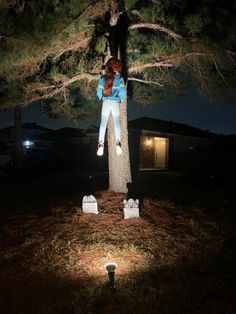 a woman standing on top of a tree in the middle of a yard at night