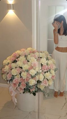 a woman standing in front of a mirror next to a large bouquet of pink and white flowers