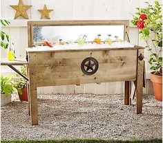 a wooden table with wheels on it in front of some potted plants and flowers