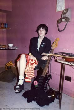 a woman sitting on the floor with a guitar in front of her and a pink wall behind her