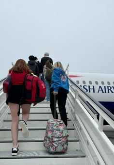 several people are walking up the stairs to board an air plane with luggage on it