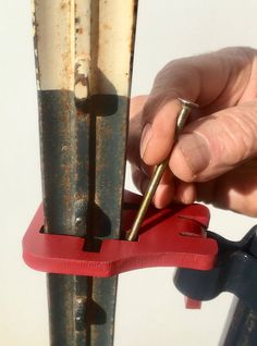 a person holding a pair of pliers in front of a piece of metal and red tape