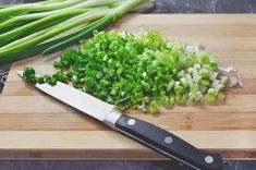 chopped green onions and celery on a cutting board with a knife next to them