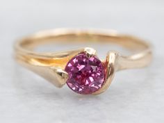 a gold ring with a pink tourmaline stone in the center, on a white surface