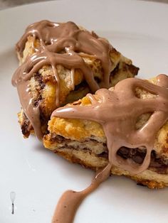 two desserts with chocolate drizzled on them sitting on a plate, ready to be eaten