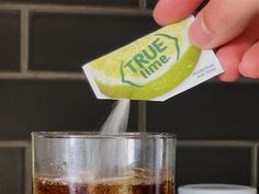 someone is pouring soda into a glass with ice cubes on the side and a sticker that says true time