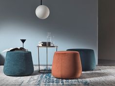 three different colored stools sitting on top of a rug in front of a gray wall