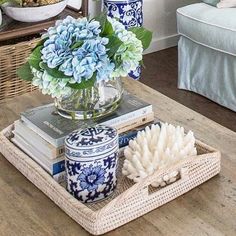 blue and white flowers are in a glass vase on a tray next to some books