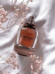 a bottle of perfume sitting on top of a white sheet next to some pink flowers