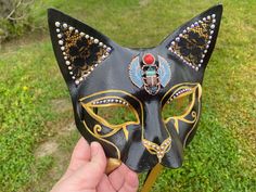 a hand holding a black cat mask with jewels on it