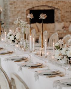 the table is set with white and gold plates, silverware, flowers and candles