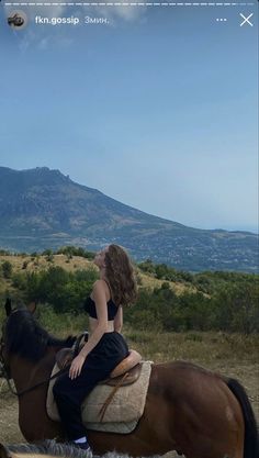 a woman riding on the back of a brown horse next to a lush green hillside