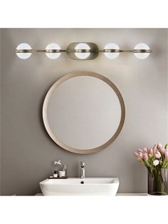 a bathroom with a sink, mirror and lights on the wall next to flowers in a vase