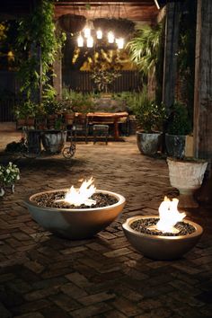 two fire pits sitting on top of a brick floor next to potted plants and lights