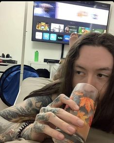 a man with long hair and tattoos holding a glass in front of his face while looking at the camera